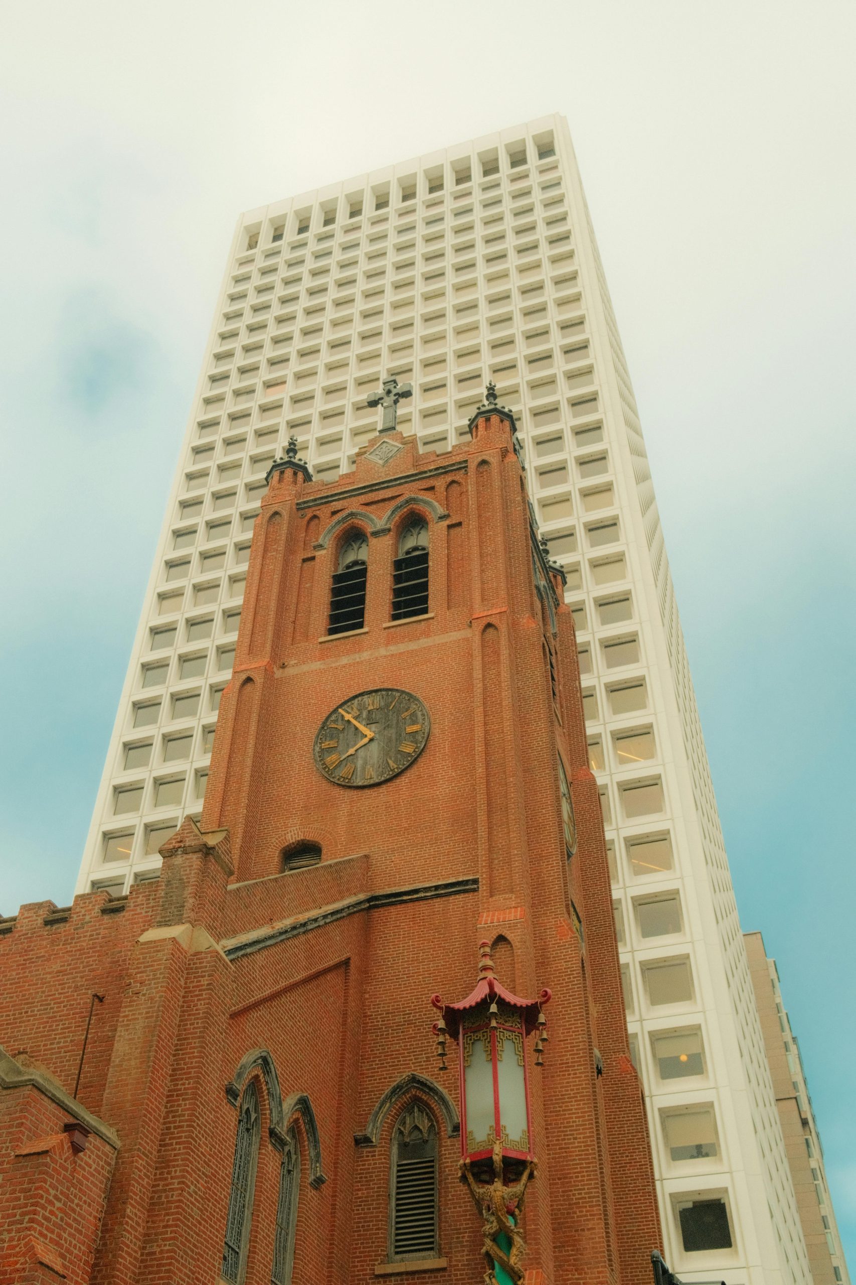 A historic church tower stands contrastingly beside a modern skyscraper under a clear sky.