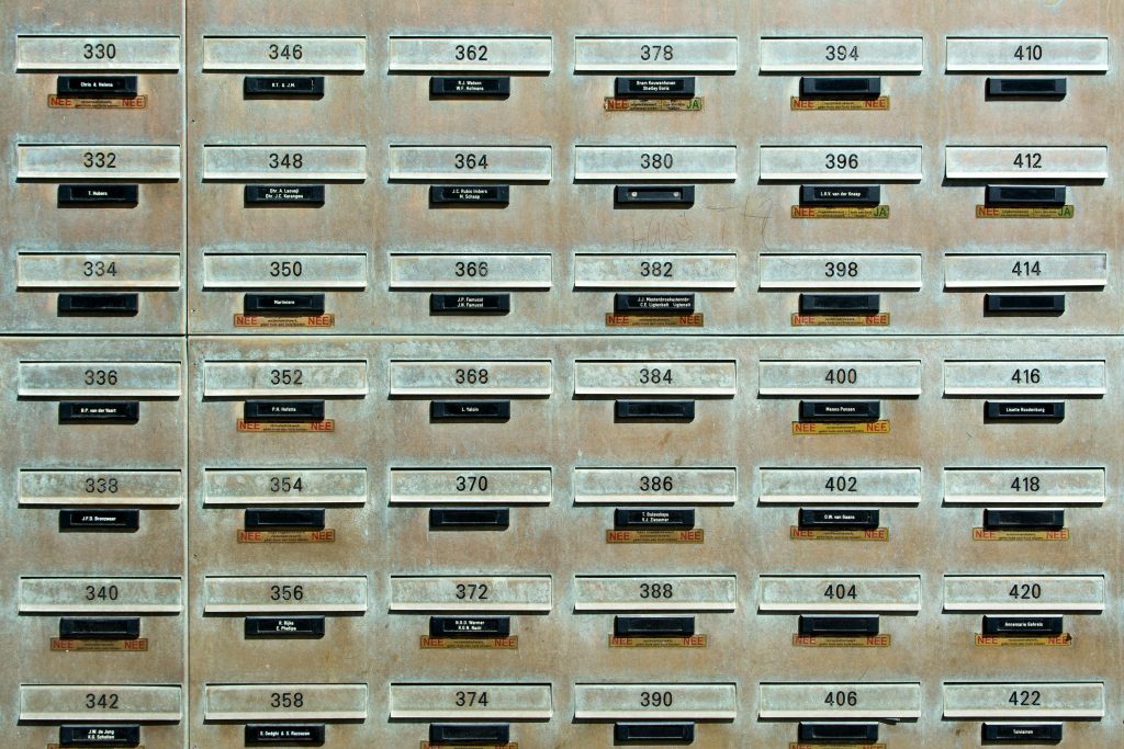Industrial metal mailboxes lined in precise rows displaying numbers, creating an urban texture.